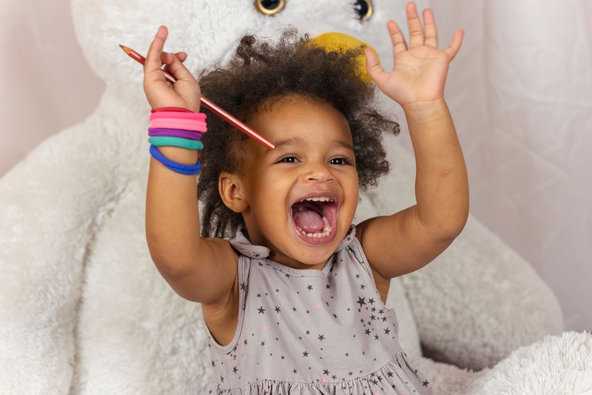 Waist-up portrait of happy african american baby girl holding hands up and laughing. Little child with wide smile